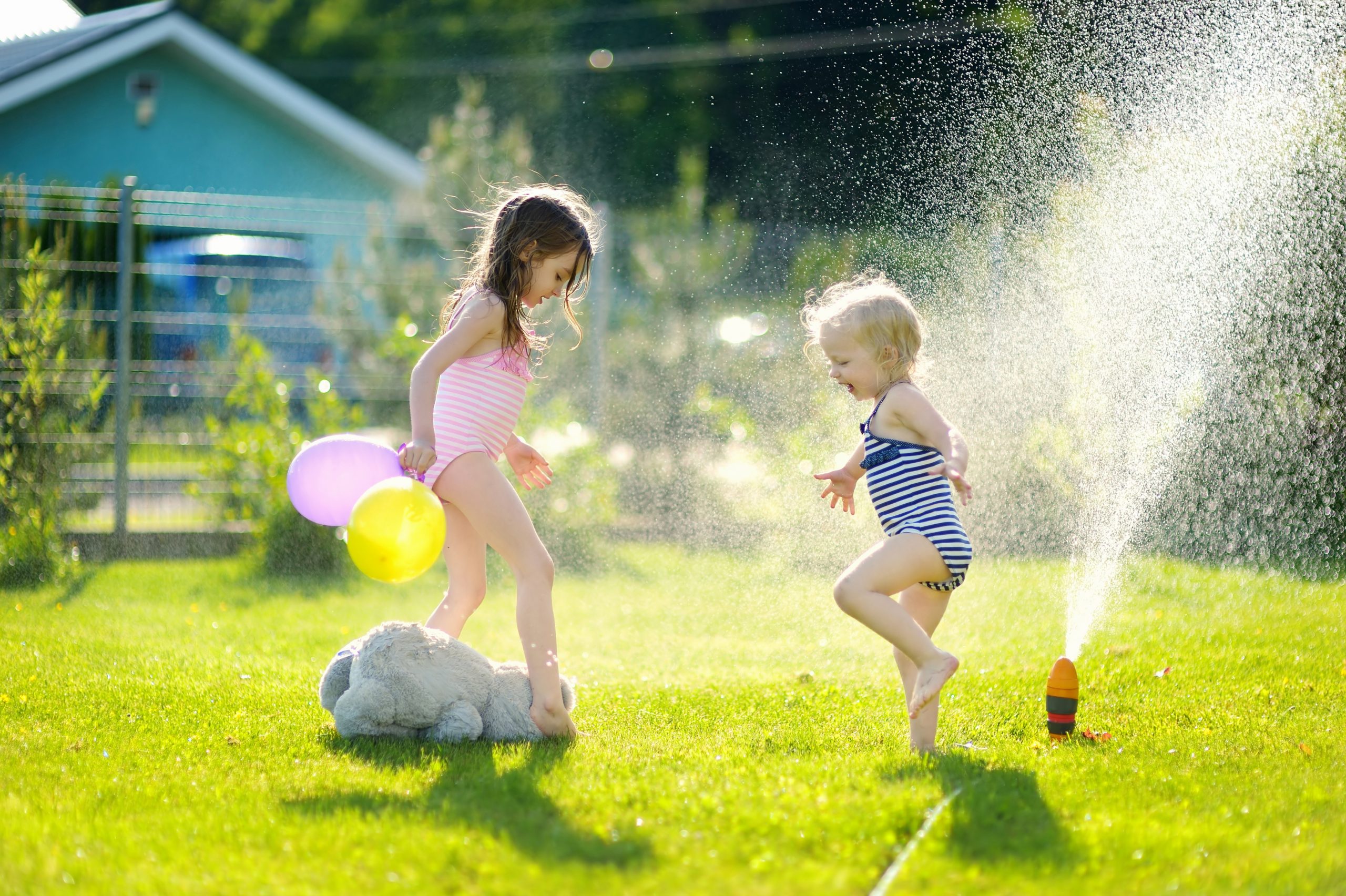 Girls running though a sprinkler in a backyard Little girls running though a sprinkler in a backyard